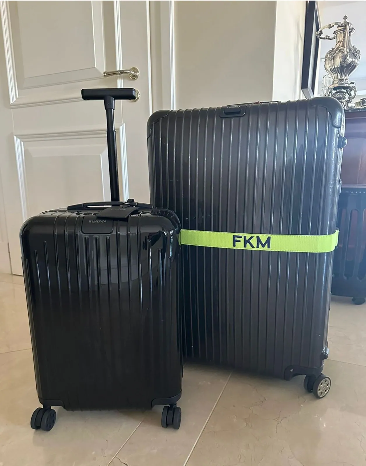 Duas malas rígidas pretas lado a lado; a maior traz uma faixa verde-limão com iniciais bordadas.